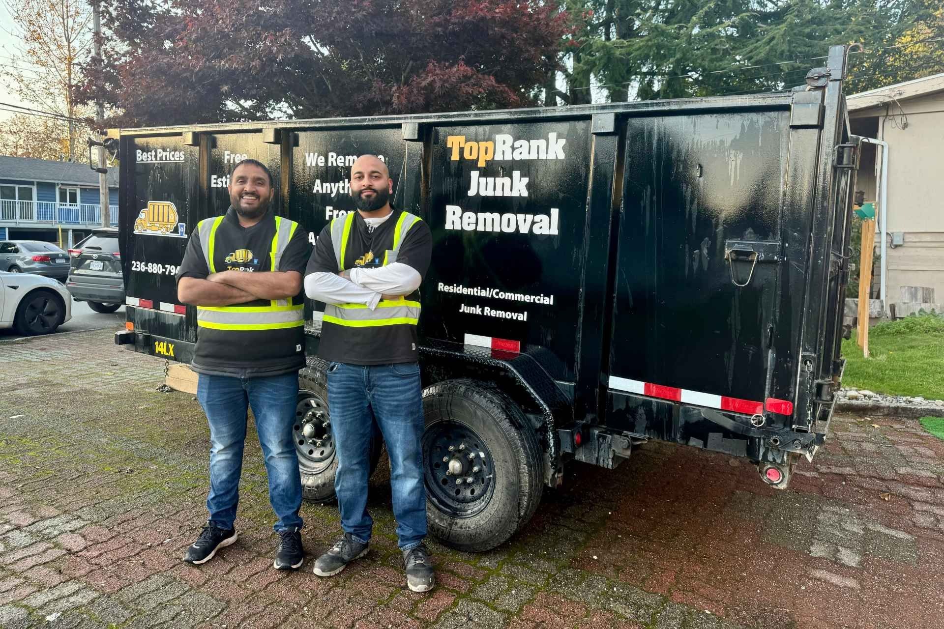 Two men pose by a junk removal trailer